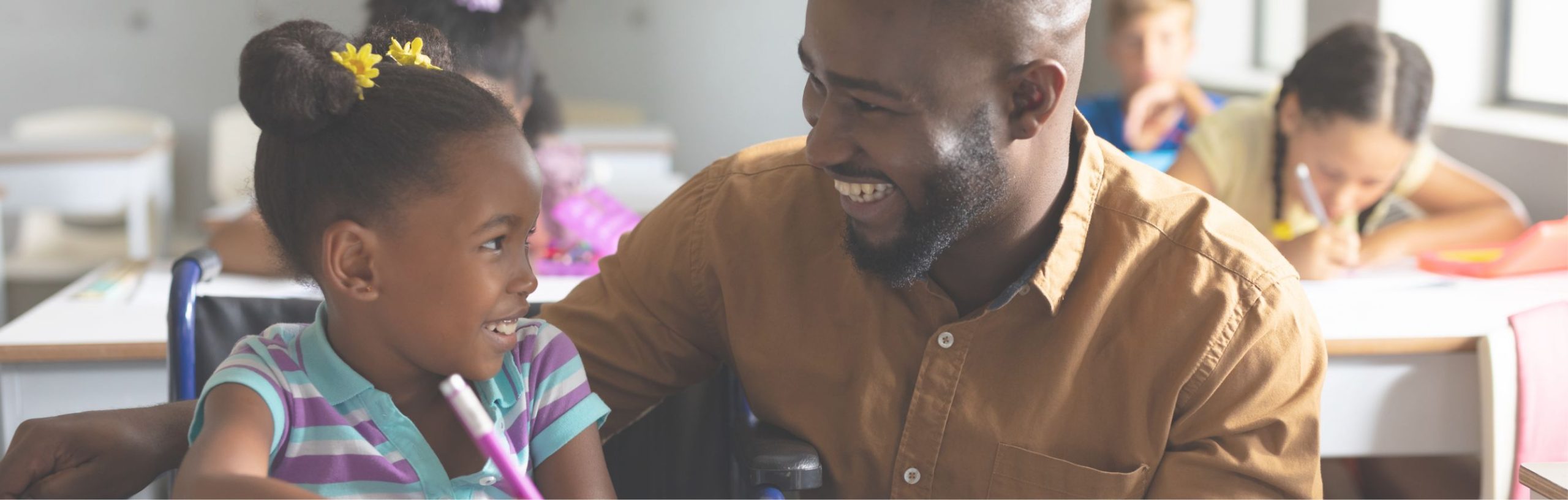 A smiling man helping a young girl with schoolwork in a classroom