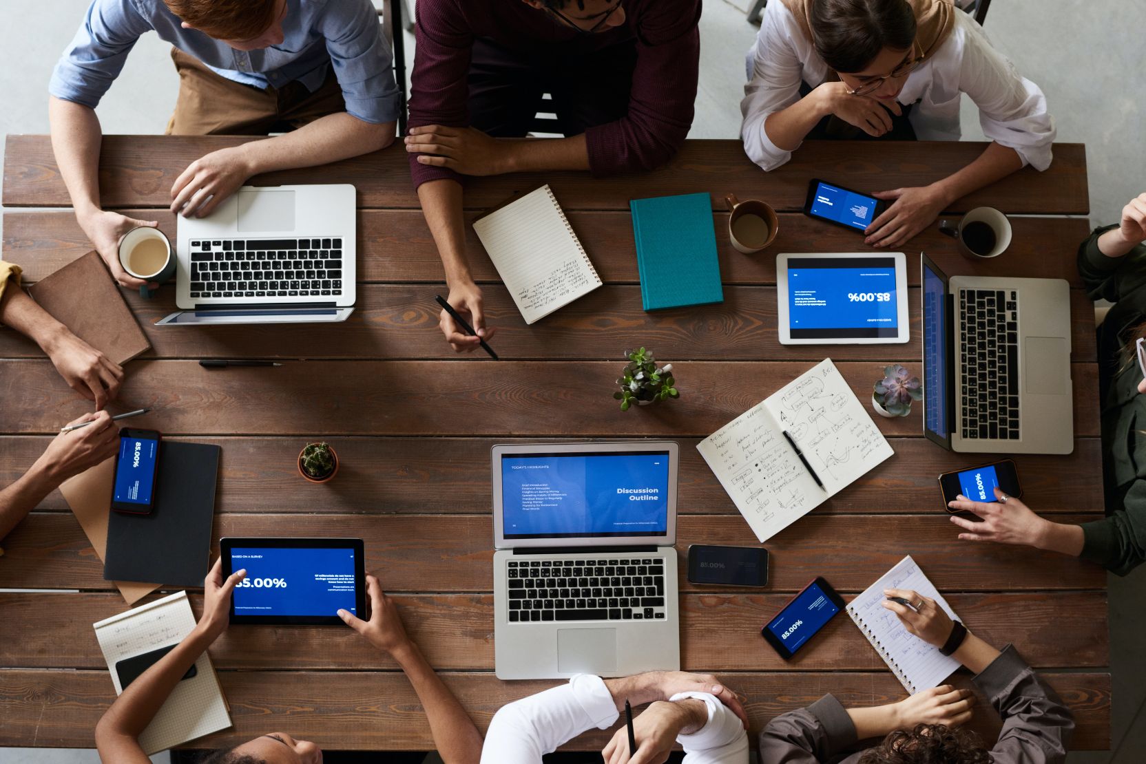 A team seen from above around a wooden table covered in laptops, tablets and notebooks