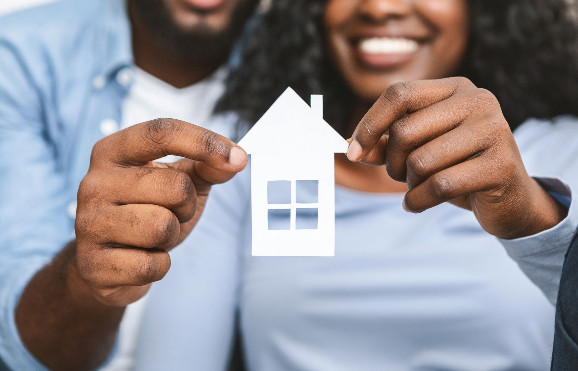 A smiling couple holding up a small white paper house