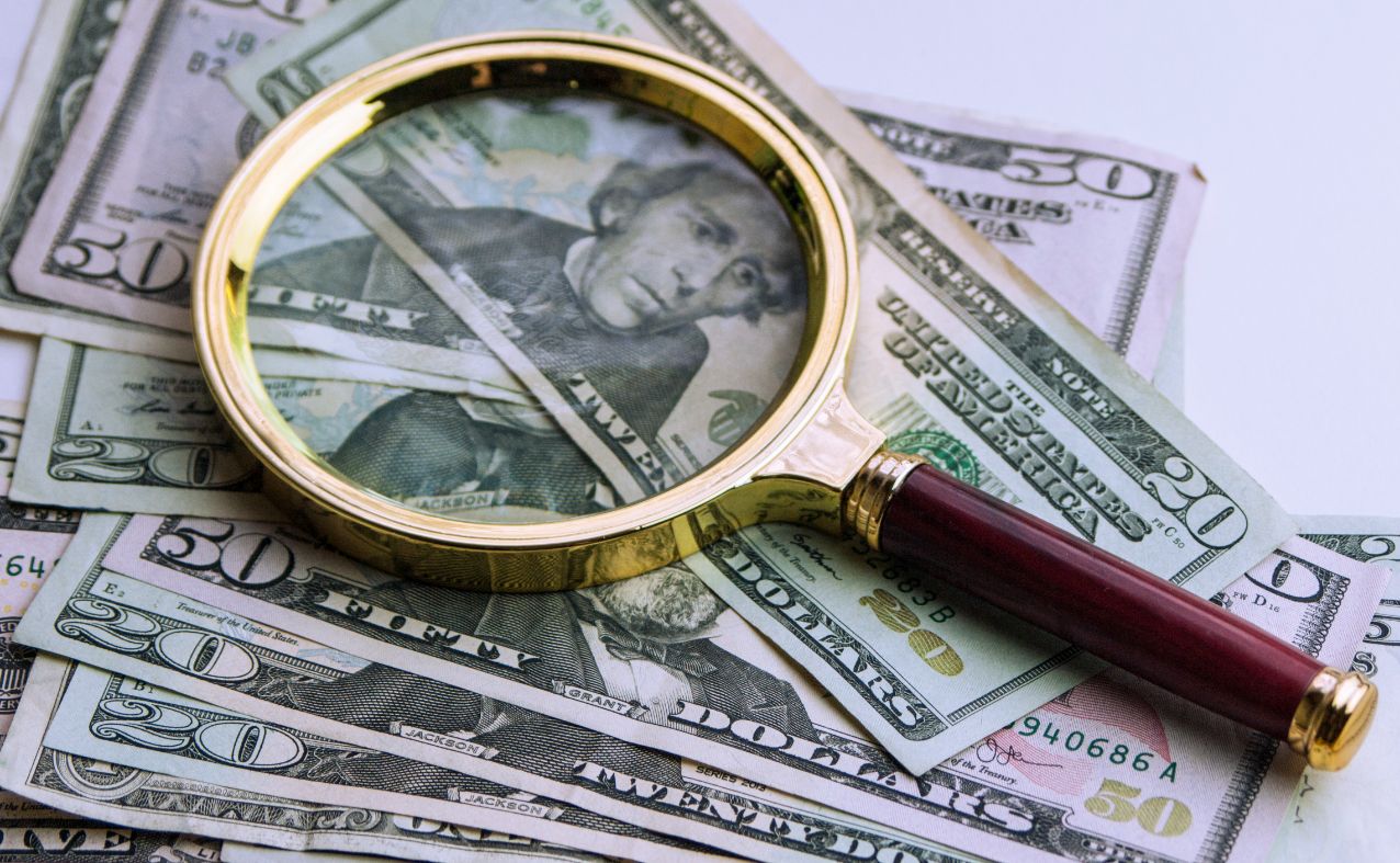 A magnifying glass resting on a spread of US dollar notes