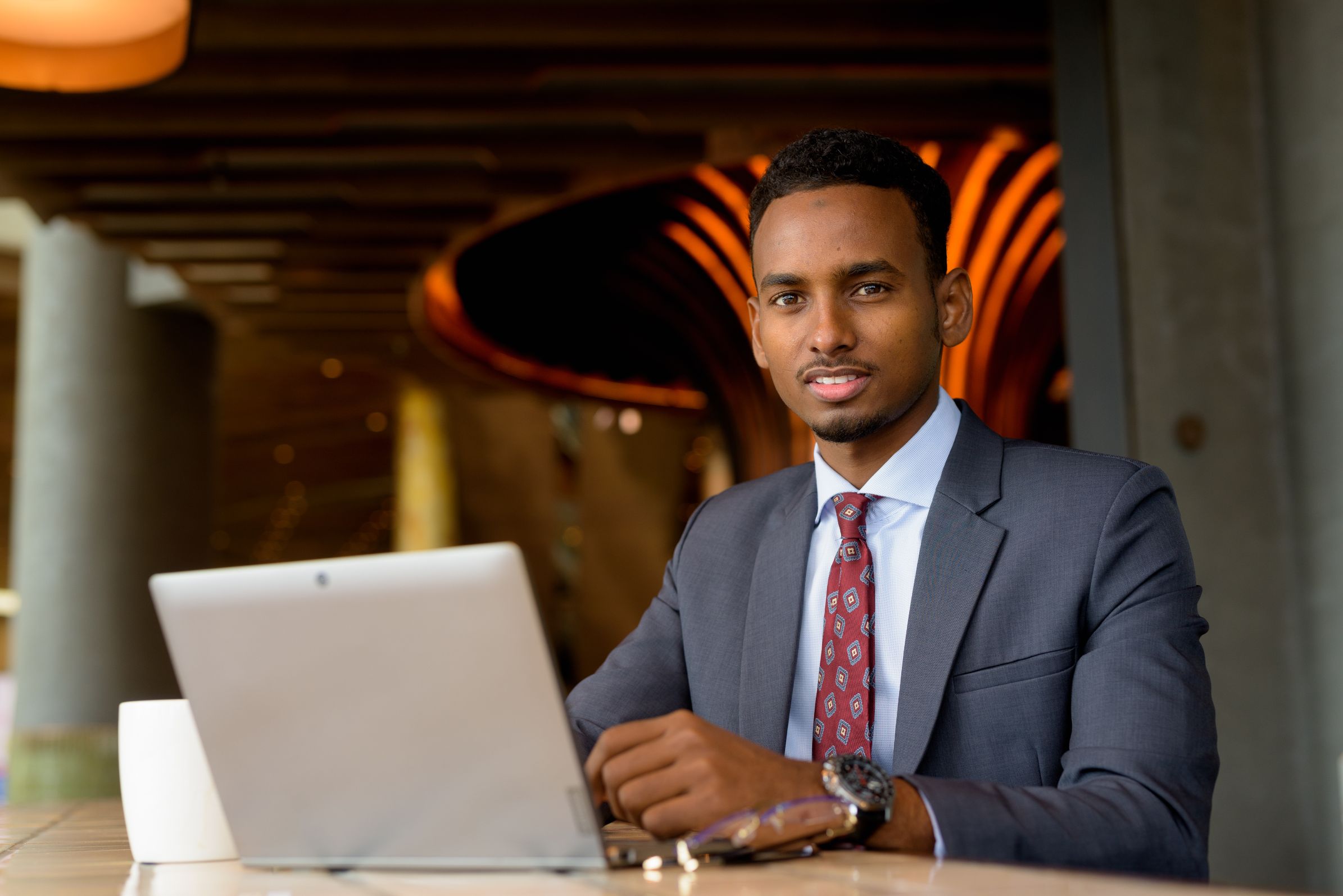 A young man in a suit and tie seated at a laptop in a modern lounge