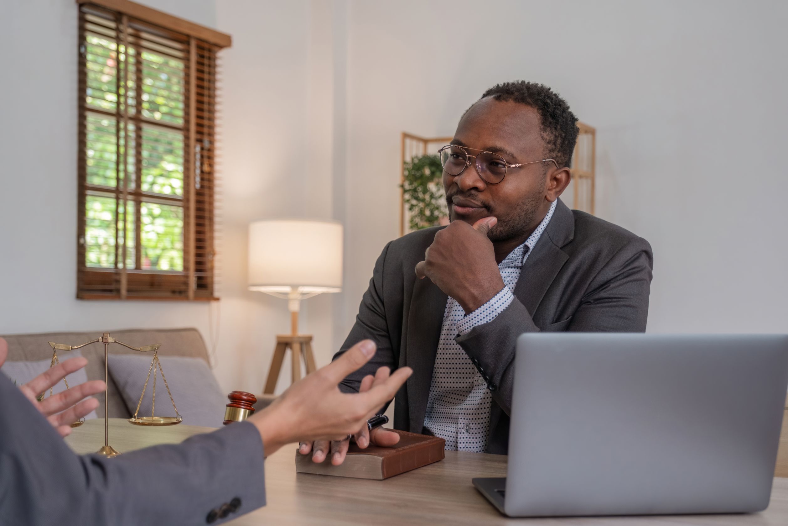 A man in a suit and glasses listening to a client across a table with a laptop