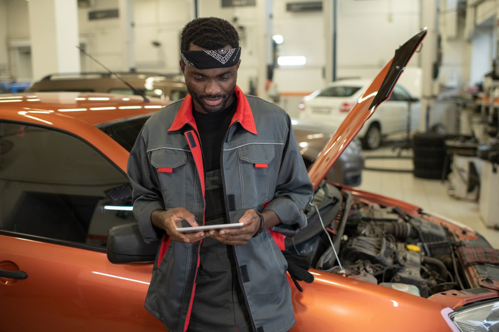 A mechanic using a tablet beside a car with its bonnet open in a garage