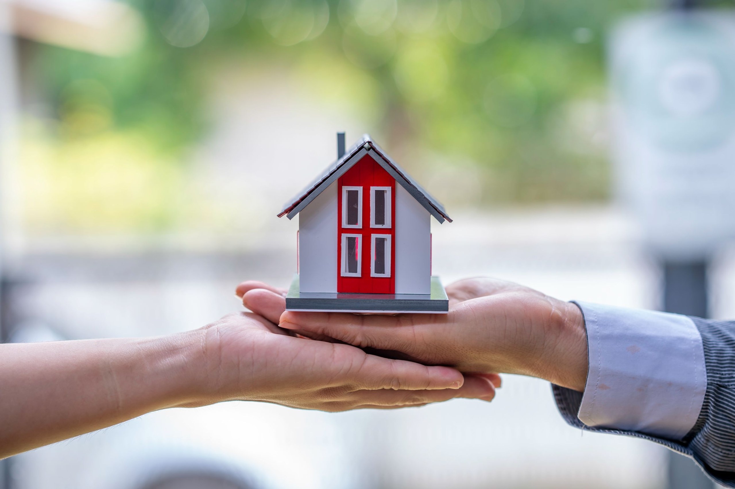 One hand passing a small model house into another's open hands
