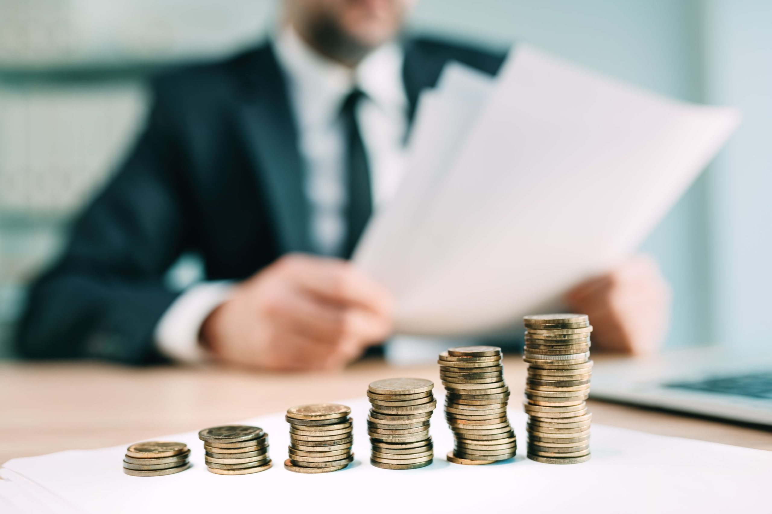 A man holding papers behind a row of rising coin stacks