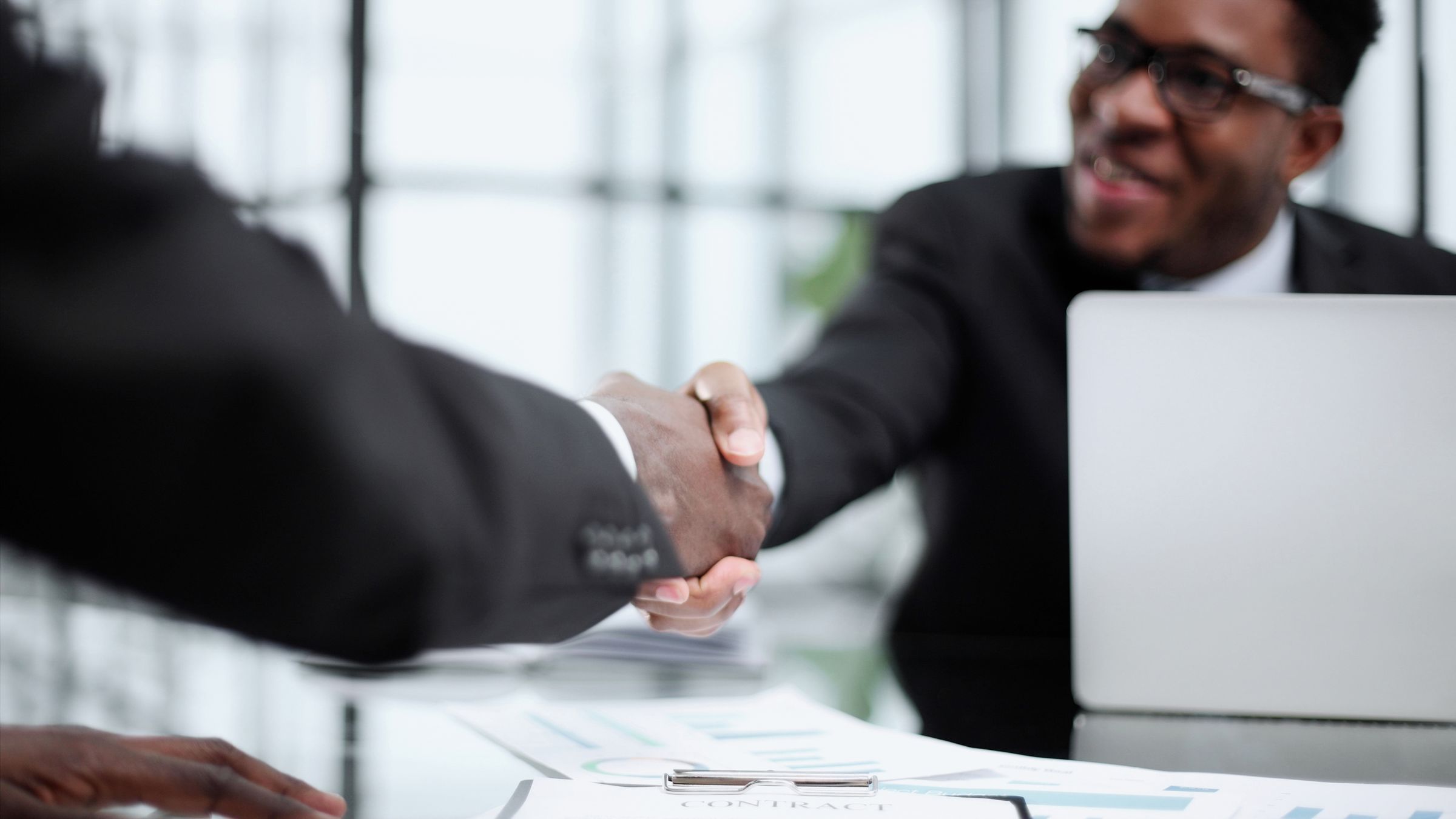 Two businessmen shaking hands across a desk in a modern office
