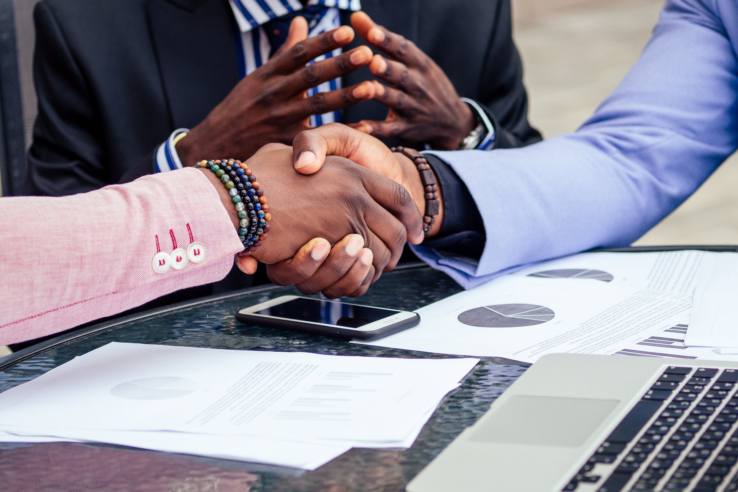 Two people shaking hands over papers and a laptop