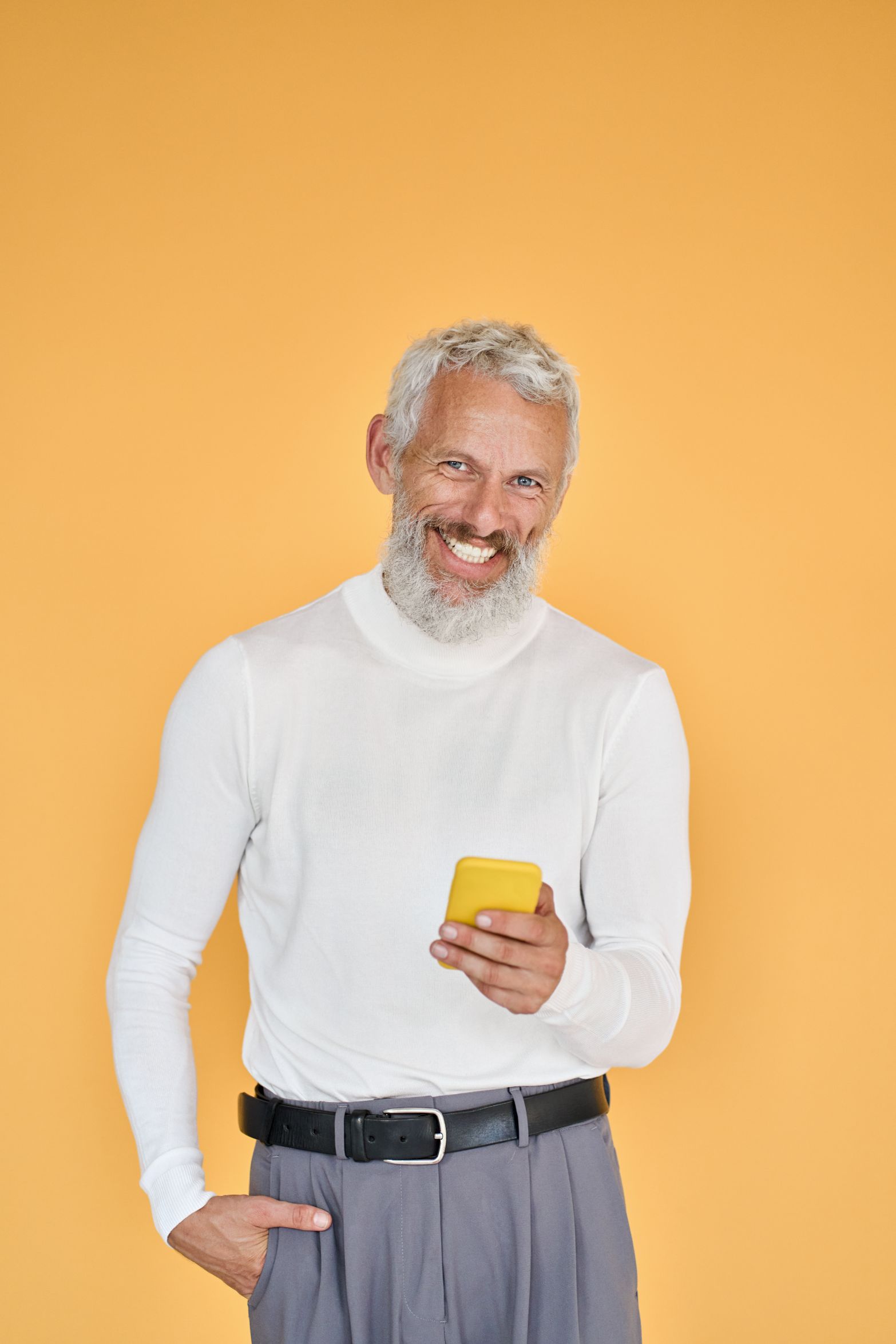 A smiling older man in a white sweater holding a smartphone