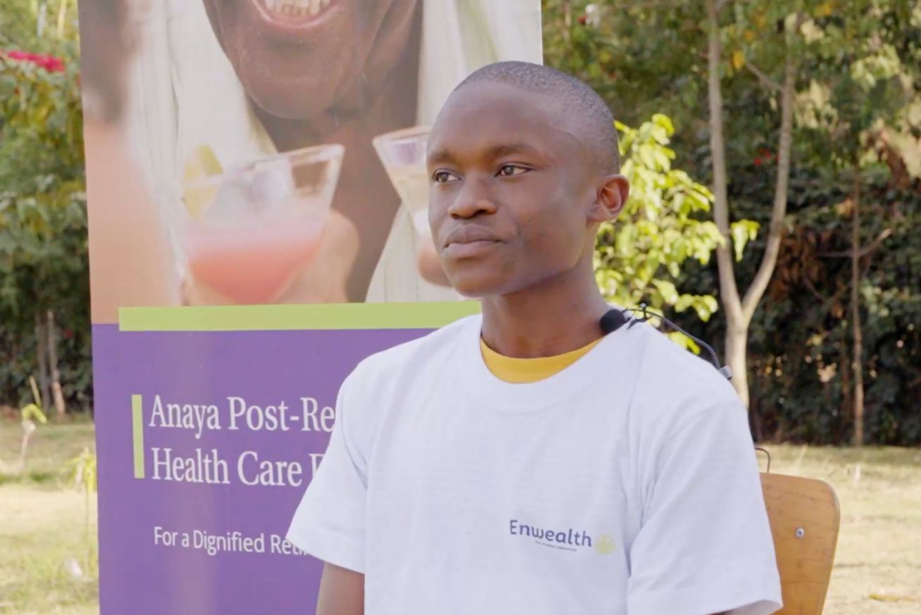 A young man in a white Enwealth t-shirt interviewed outdoors in front of an Anaya Post-Retirement Health Care banner
