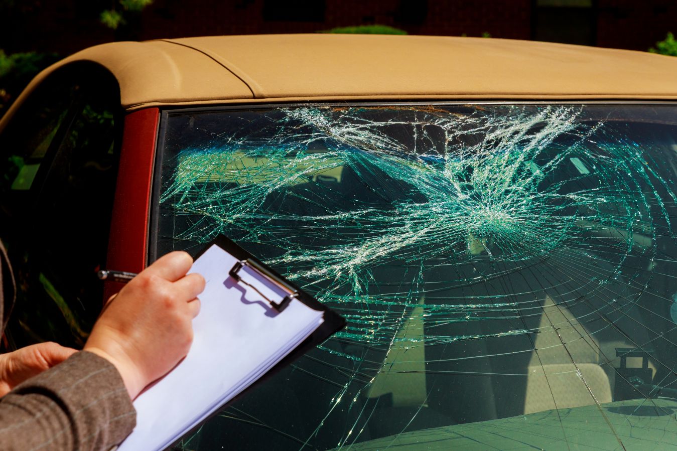 An assessor writing on a clipboard beside a car with a shattered windscreen