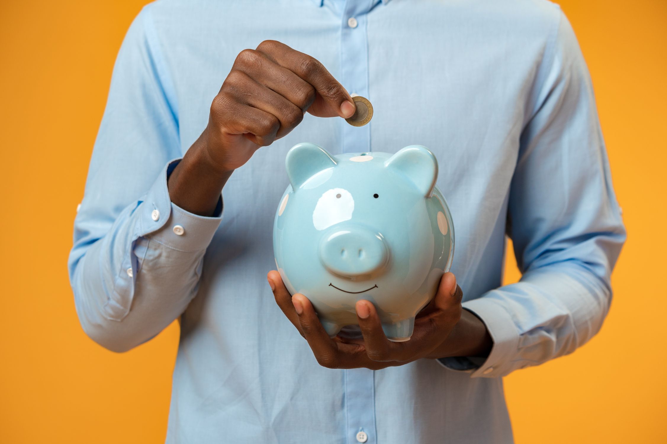 A man in a blue shirt dropping a coin into a piggy bank