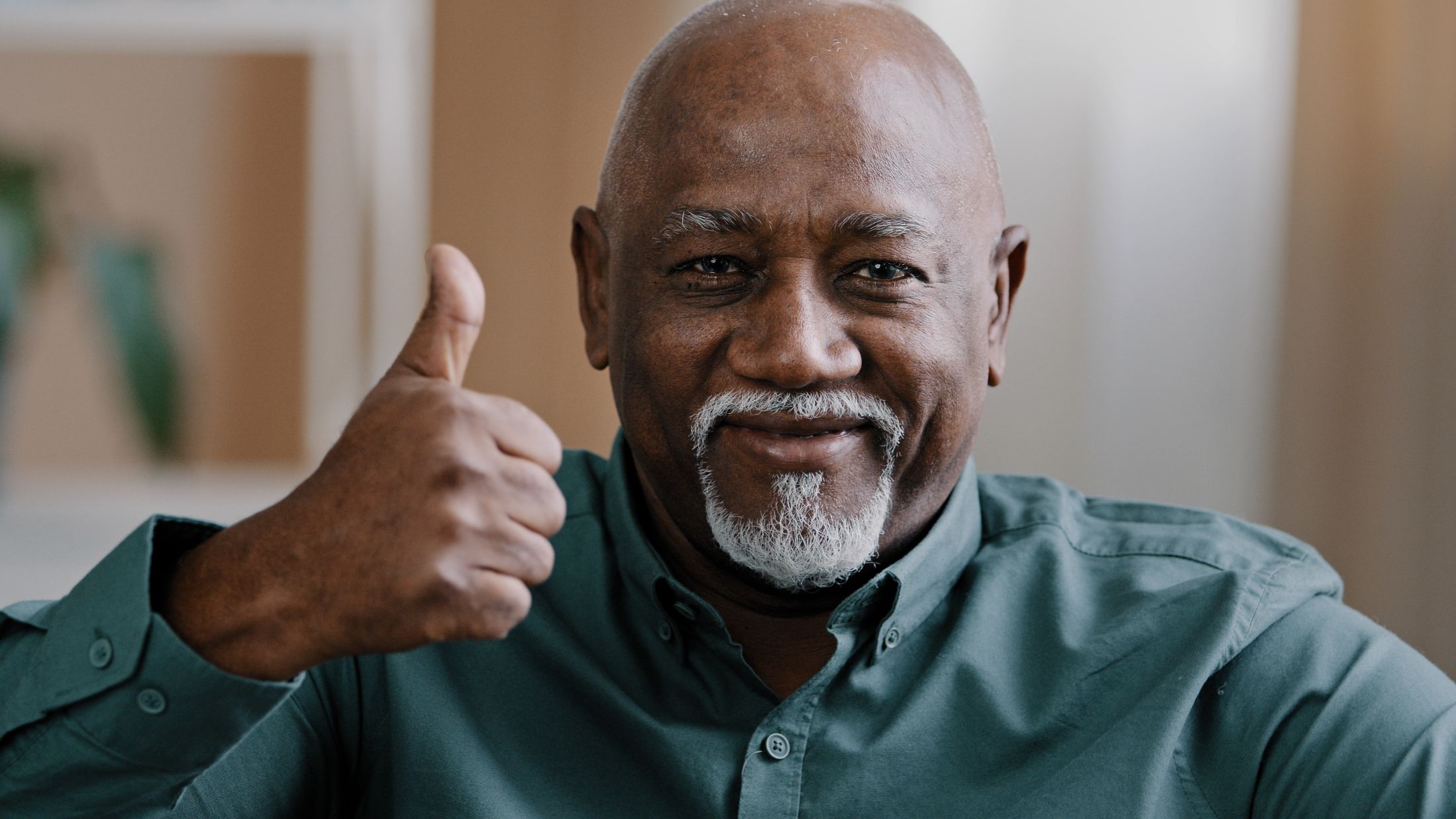 An older man in a green shirt smiling and giving a thumbs up