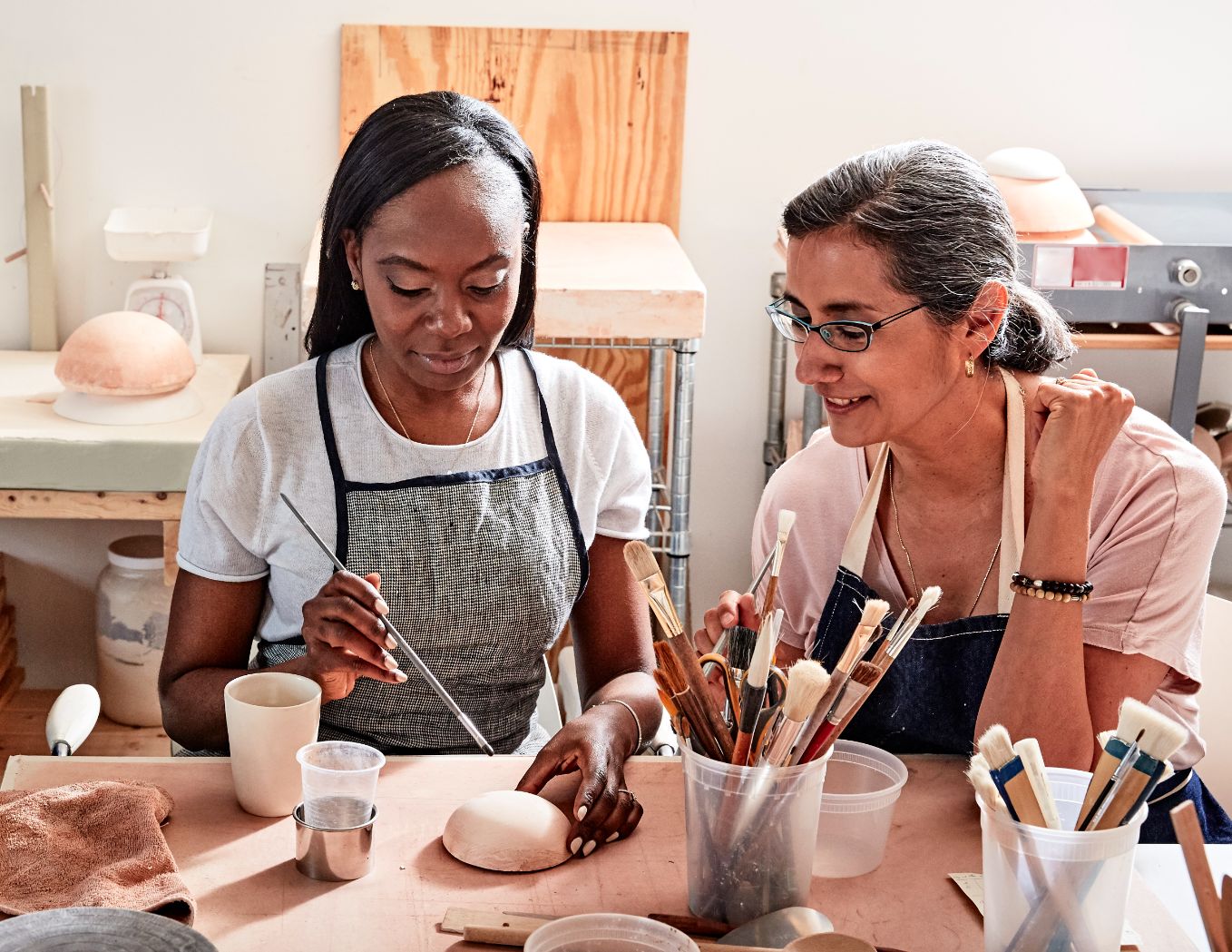 Two women painting pottery together at a studio table