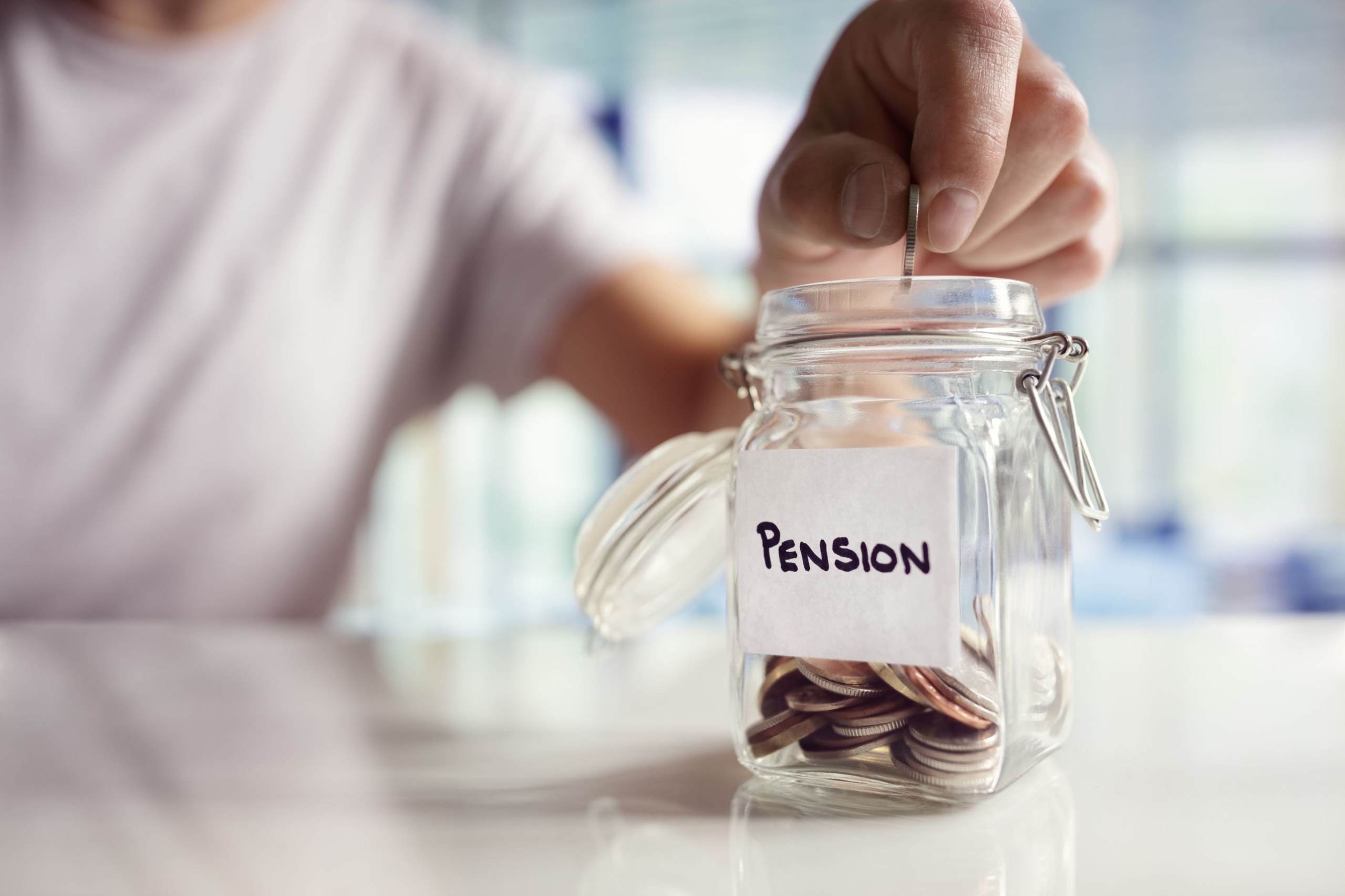 A hand dropping a coin into a glass jar labelled Pension