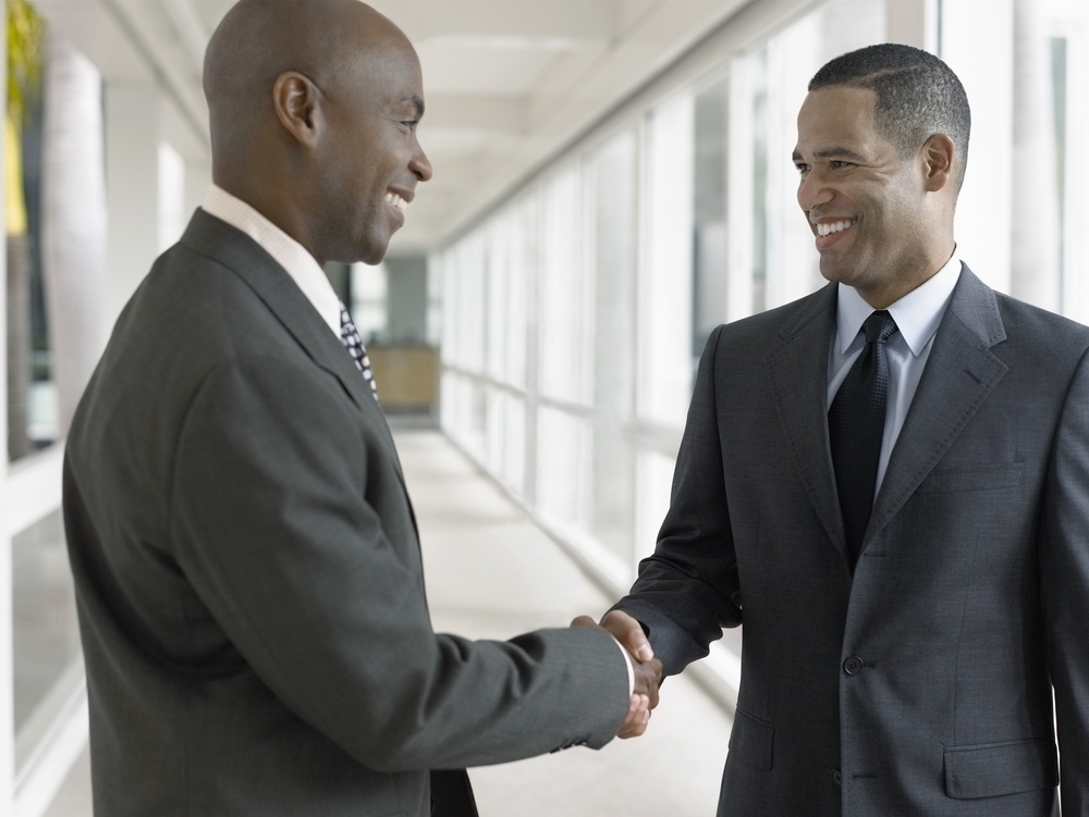 Two businessmen in suits shaking hands in a bright corridor