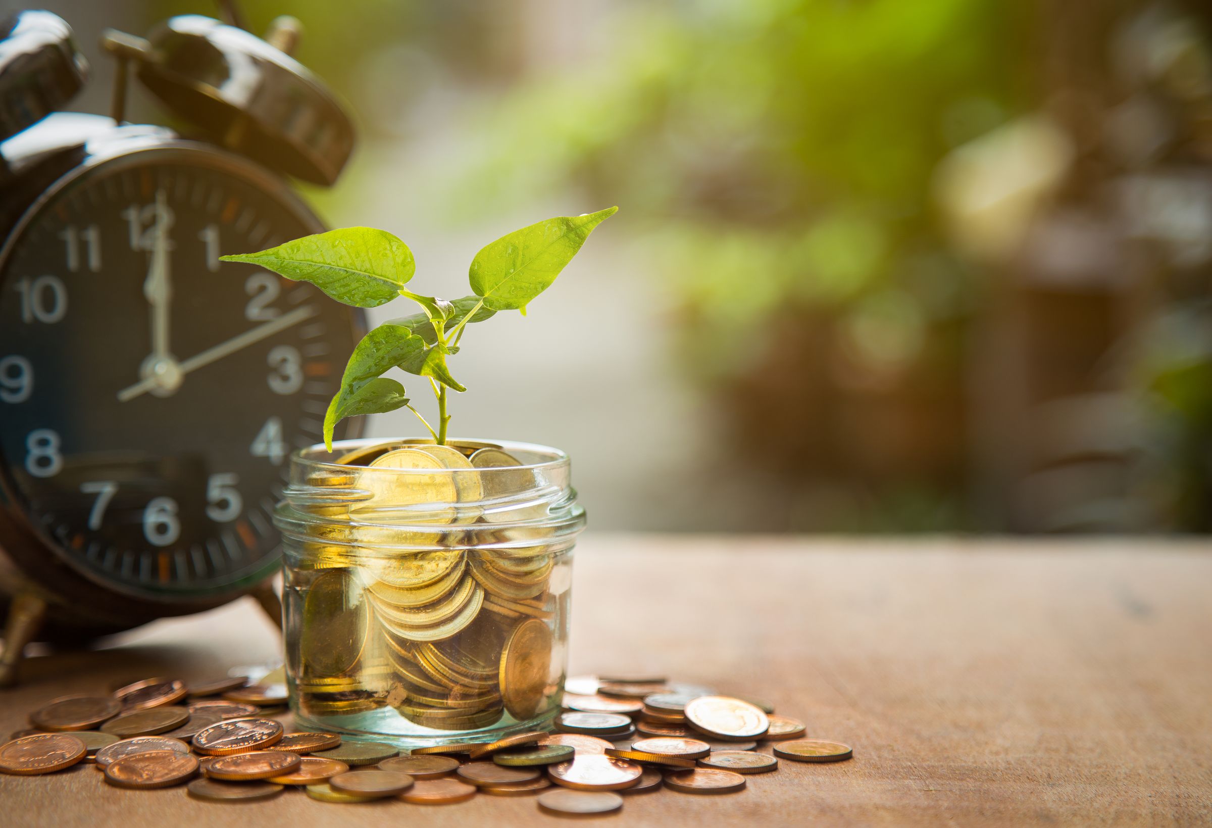 A seedling growing from a jar of coins beside an alarm clock