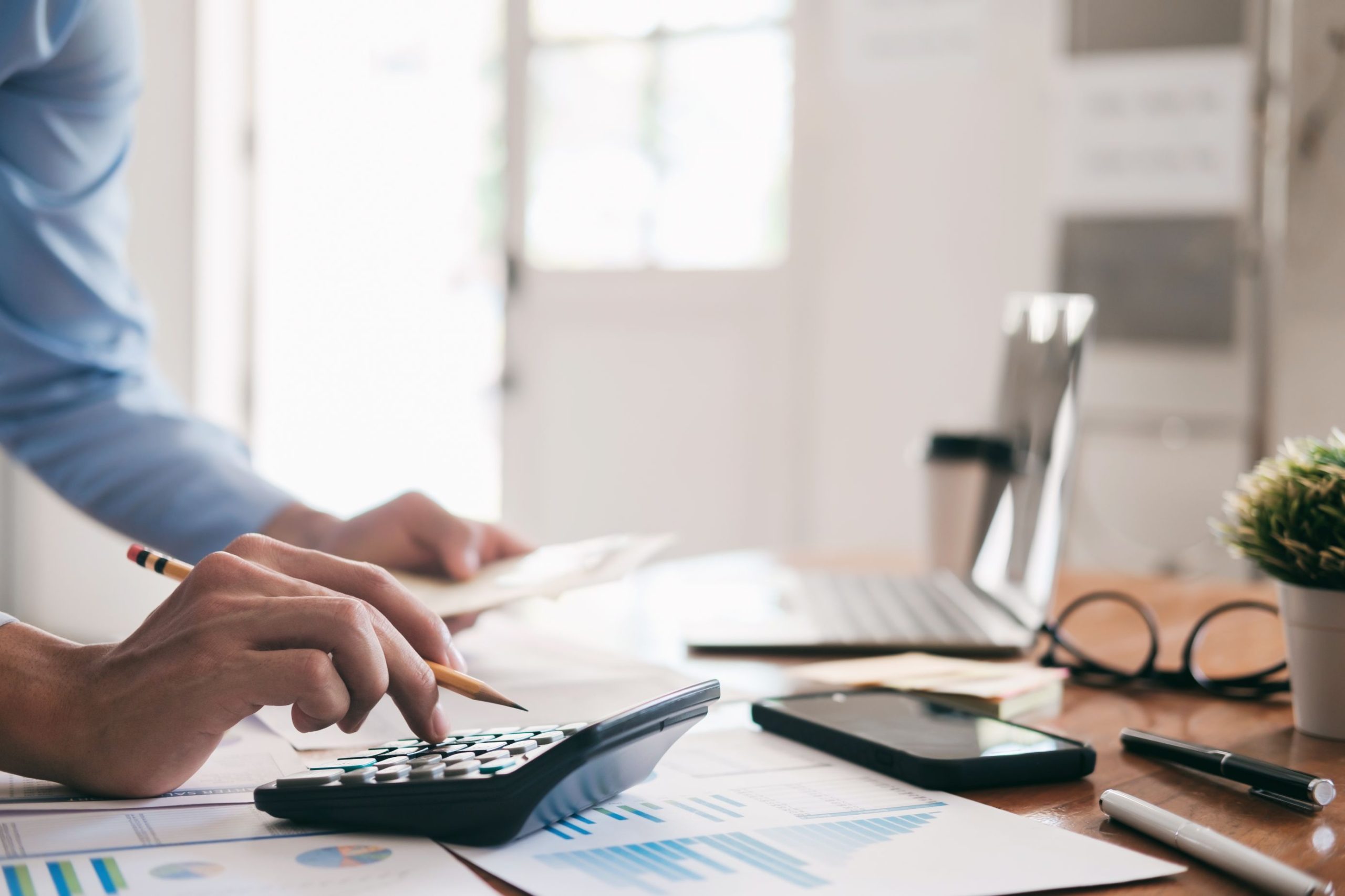 Hands working a calculator over printed charts at a desk