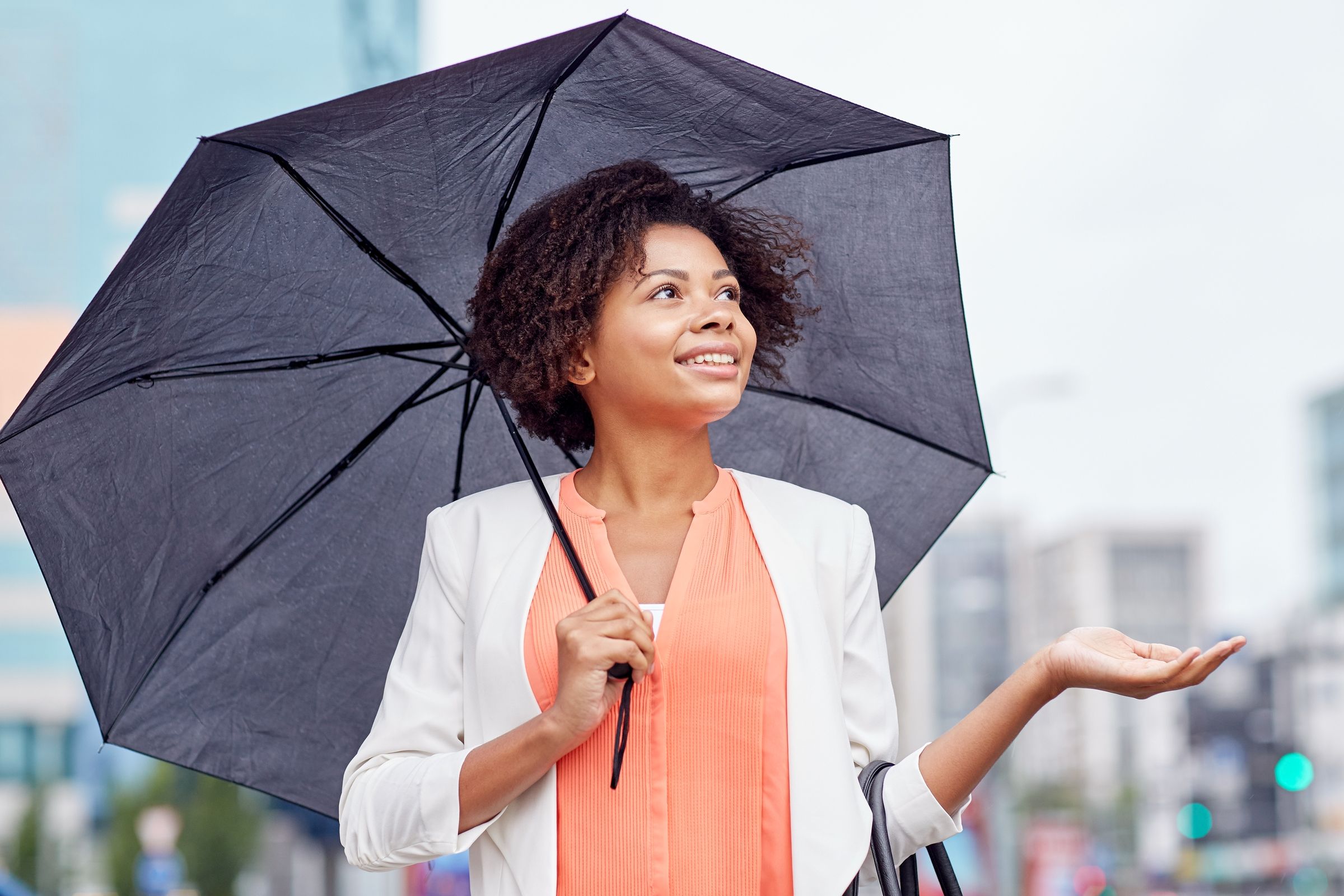 A smiling woman under an umbrella on a city street